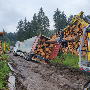 Mit Bagger und montiertem Mehrzweckgreifer zieht die Holzstämme aus dem Container