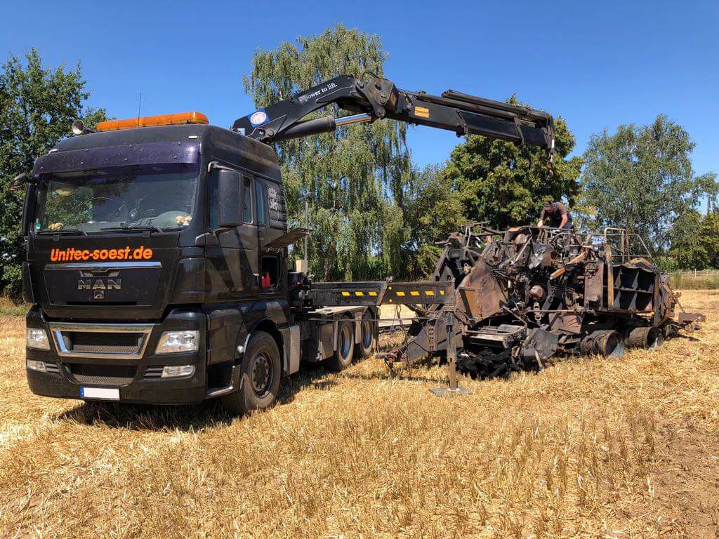 Ein MAN-Lkw mit Kran, der eine beschädigte Maschine auf einem Feld hebt.